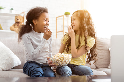 School aged kids sitting on sofa and eating popcorn during a playdate. Kids & their friends are safer when hazardous items are locked in Forti Goods furniture.