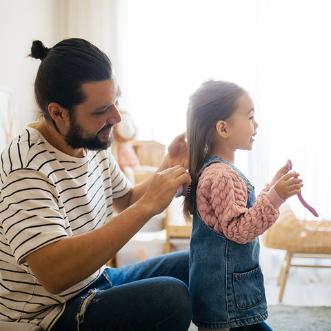 Father brushing toddler daughter's long hair before a playdate.