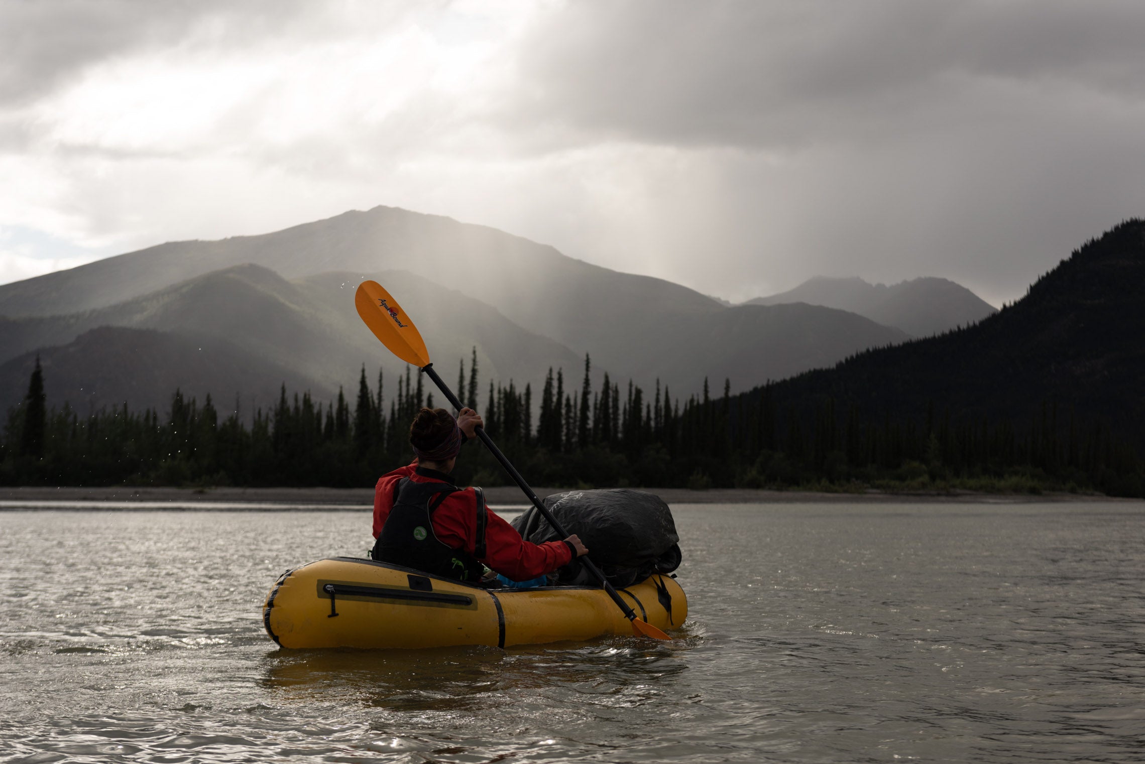 Person packrafting with gear in a lake with a mountain in the background