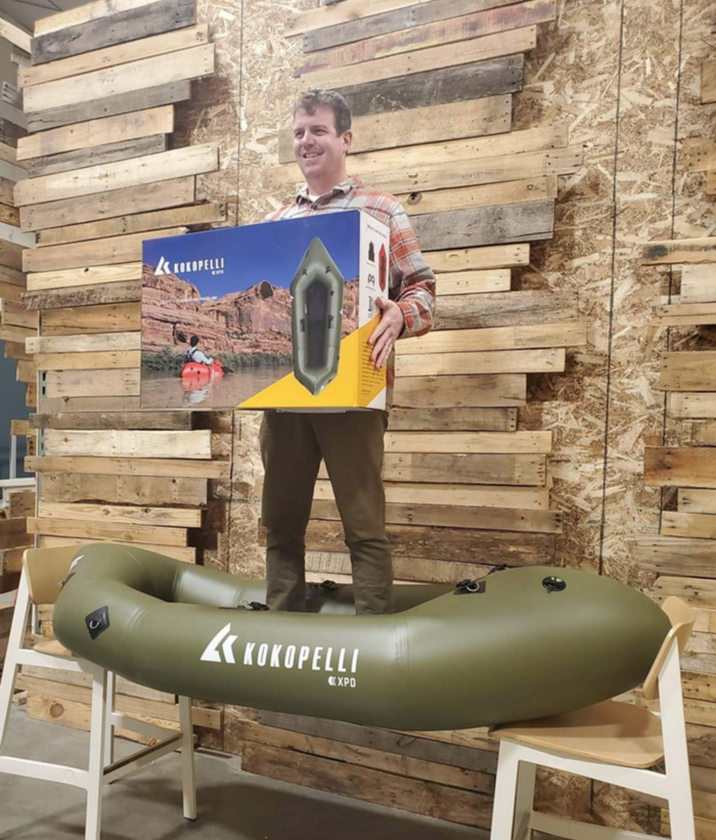 Man standing inside an XPD Kokopelli Packraft supported by two chairs