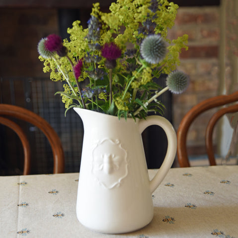 alt="White ceramic jug filled with flowers on kitchen table"