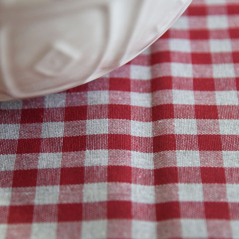 A large cream mixing bowl on red gingham oilcloth