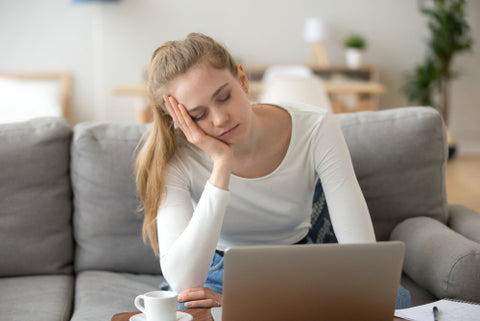 Woman holds her head while sitting on a couch as if tired