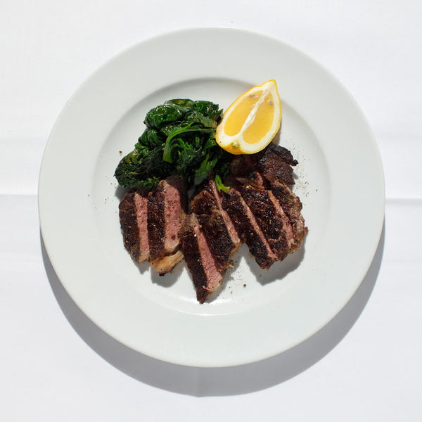 Sliced sirloin steak with a lemon wedge and braised spinach.