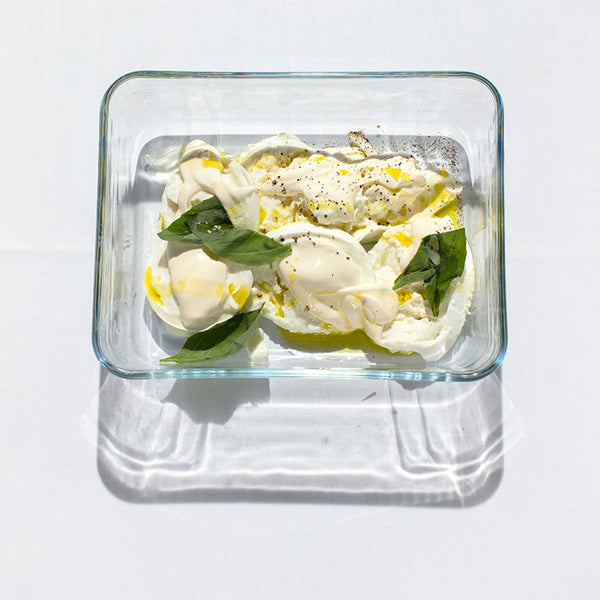 Mozzarella di Bufala, creme fraiche and basil leaves in a pyrex dish.