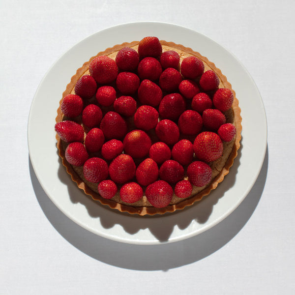 Frangipane almond tart topped with strawberries served on a white plate.
