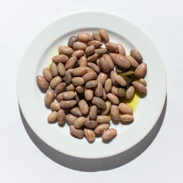 Fresh borlotti beans with sage and a drizzle of olive oil on a white plate.