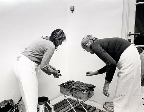 Black and white image of Ruthie Rogers and Rose Gray, founders of the River Cafe, cooking outside on a metal grill