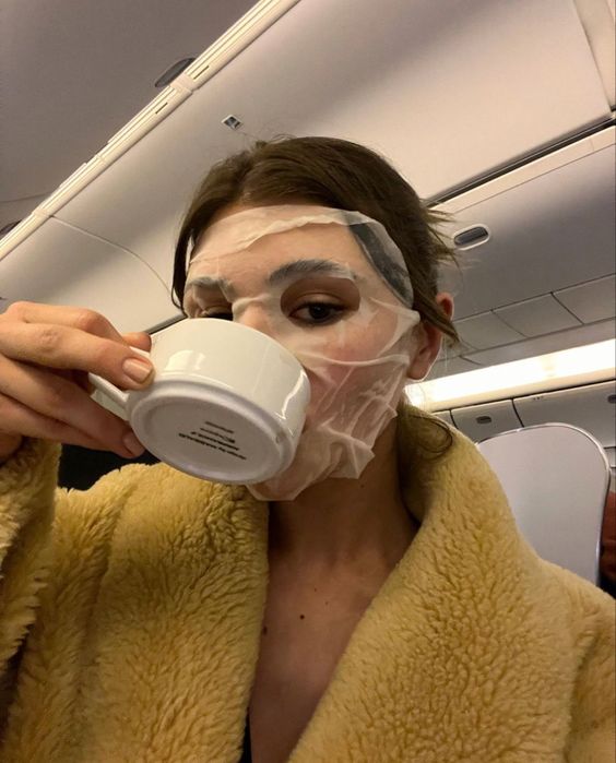 Lady with a face mask drinking coffee on a plane
