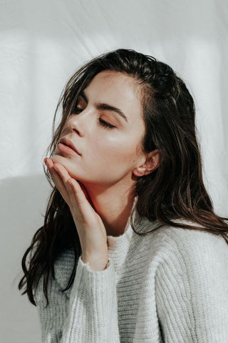 dark haired girl in a white sweater holding her hand on her chin