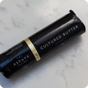 Black package of cultured butter on a marble surface.