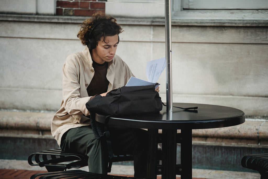 A Young Man reading the book beside One black Table with Umbrella, Sitting on Long Metal Chair