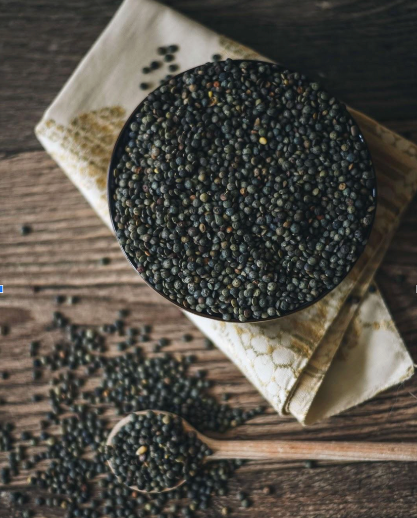 Raw black lentils in a bowl with a spoon