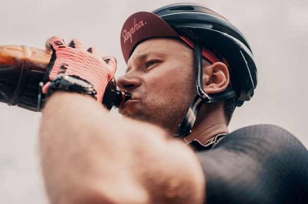 Close-up of a man with a bike helmet and gloves drinking out of a bottle