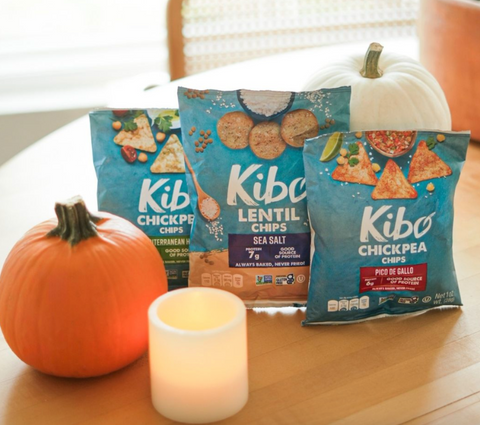 Kibo Chickpea Chips and Lentil Chips arranged on a dining table with small pumpkins and a candle