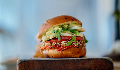A gourmet veggie burger with arugula and tomato sits atop a wooden cutting board