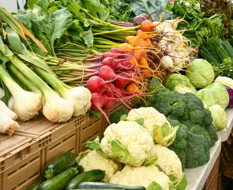 Fresh vegetables like radishes and cauliflower are arranged on a farmer's market stand