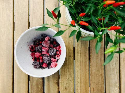 Mixed frozen berries in a bowl on a wooden surface next to a plant