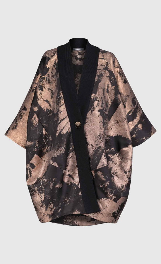 Front view of the Alembika Bronze Jacket. This jacket is black with a metallic bronze print on it. The jacket goes down to the knees and has 3/4 length sleeves, two front pockets, and a single button front.