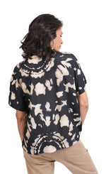 Load image into Gallery viewer, Back top half view of a woman wearing khaki pants and the alembika speckle mandala shirt. This shirt has a black and white mandala tie dye print, a boxy silhouette, and short sleeves.
