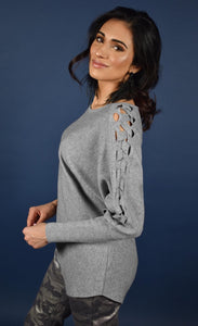 Left side top half view of a woman wearing the frank lyman grey knit sweater. This sweater has long sleeves with a braided detail running down the sides. 