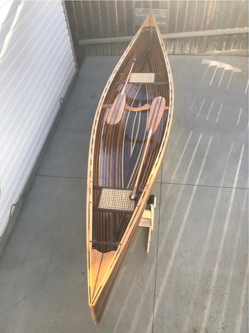 A view down the length of a wooden canoe, with two paddles laid across it in opposite directions