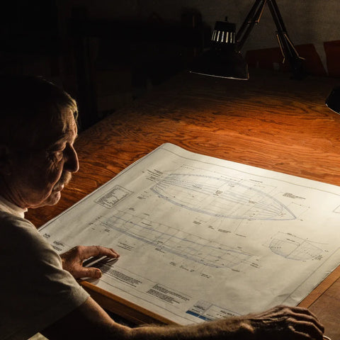 A man reviews plans for a wooden skiff