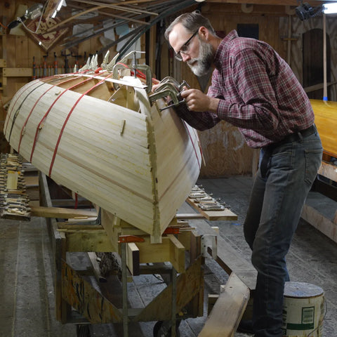 A man adjusts a clamp on a partially planked skiff