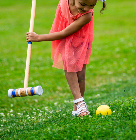 A little girl playing croquet, a traditional English lawn game that requires mallets and balls