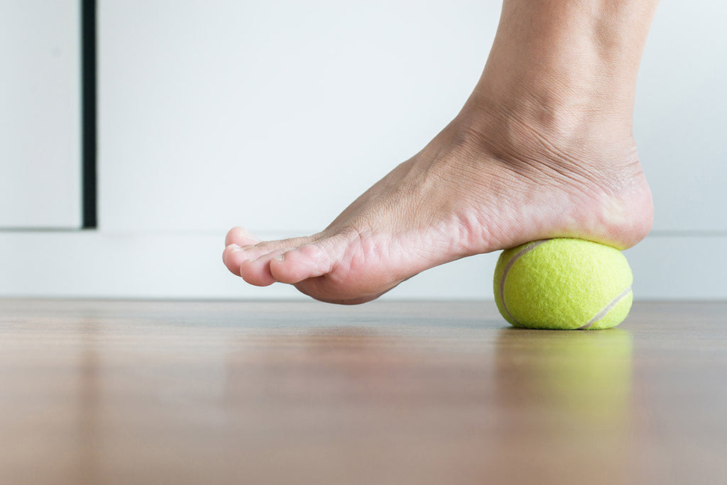 man rolling a tennis ball under foot