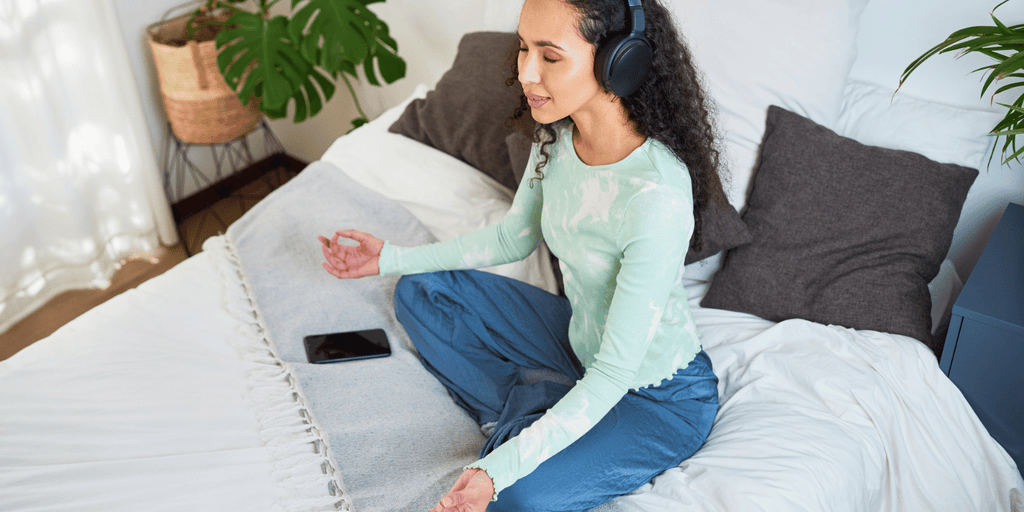 girl meditating on bed eyes closed with headphones on dark brown curly hair multi-ethnic