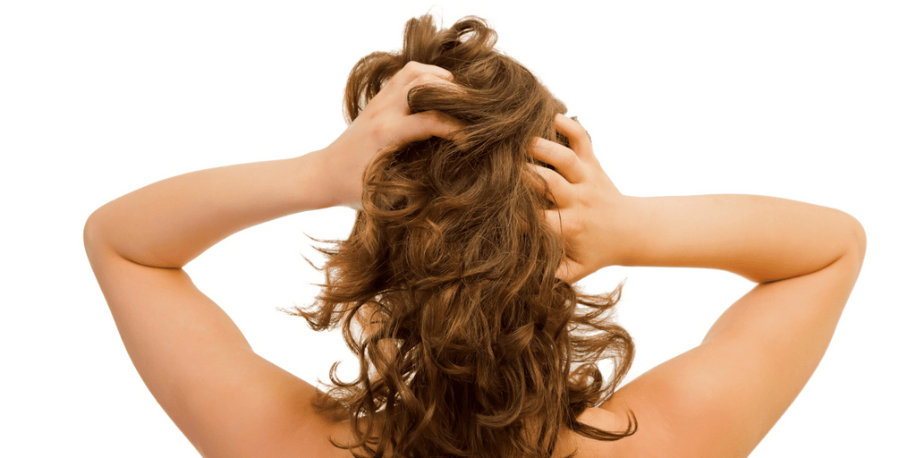 brunette woman with curly hair massaging her scalp