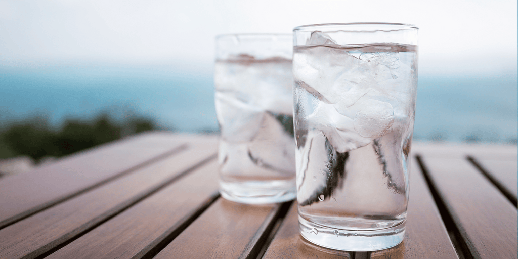 two glasses of water on a wood table with ocean in background