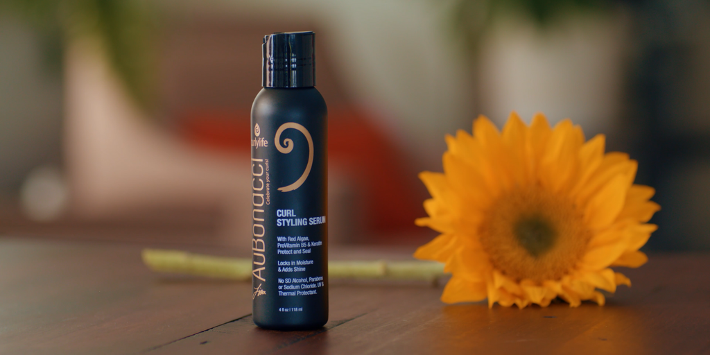 AuBonacci Curl Styling Serum with a sunflower on a wood table