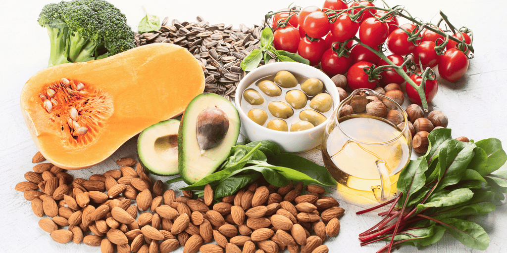 Photograph of food that is rich in vitamin E featuring melon, avocado, cherry tomatoes, almonds, spinach, olives, sunflower seeds