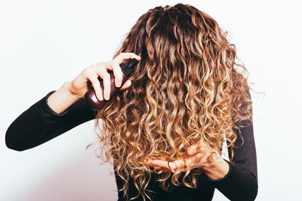 woman with curly hair spraying her hair with water