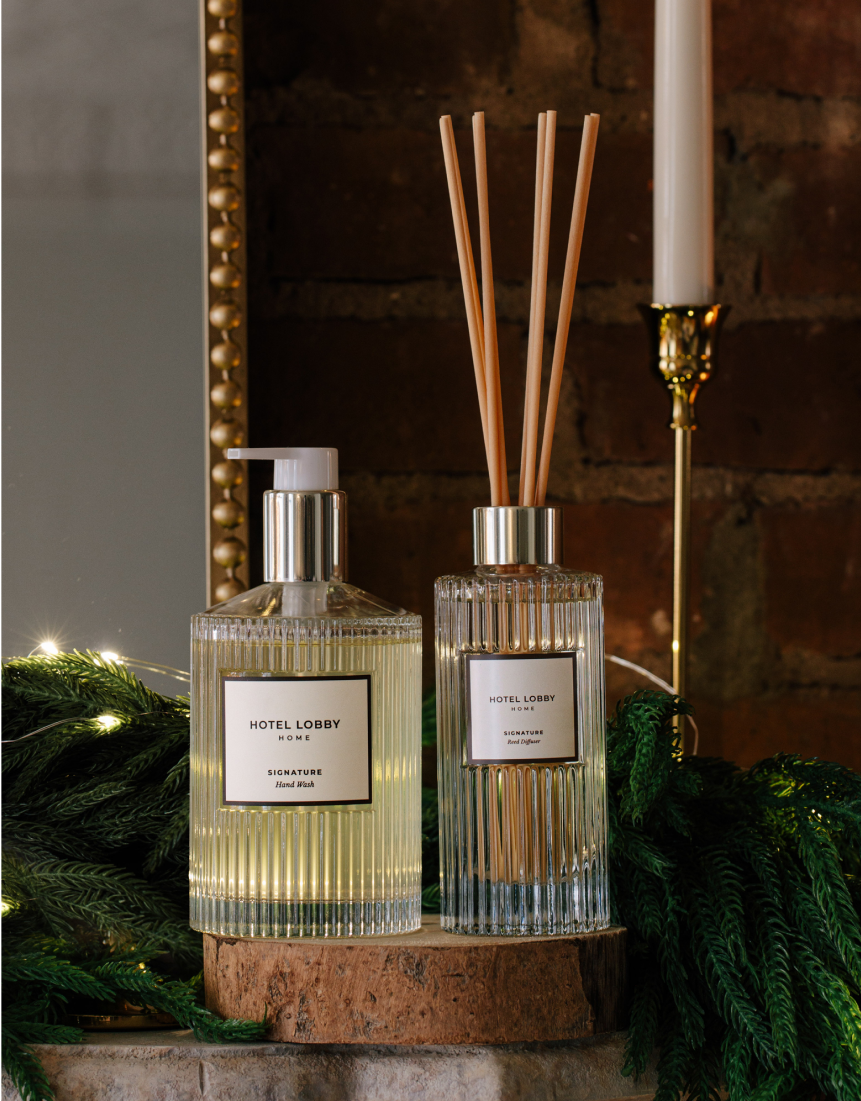 Elegant candle and fragrance bottles on a decorative mantle with green foliage.