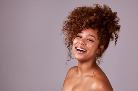 A person with a curly ponytail laughing at the camera