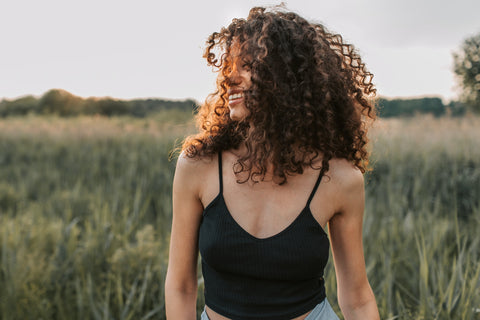 Woman with healthy curly brown hair smiling in a field