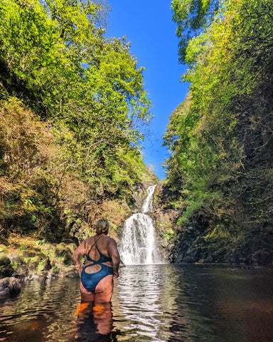 A woman wearing a swimsuit cold water swimming in a waterfall. 