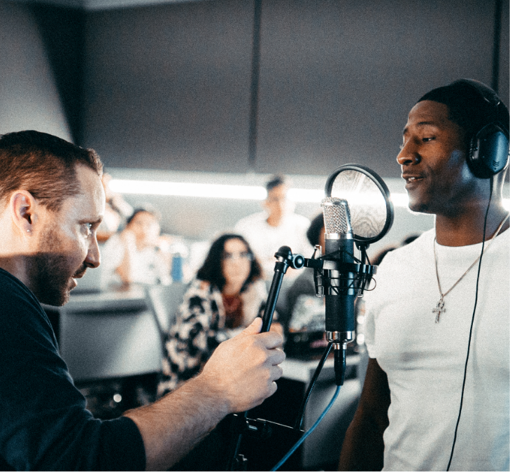 man singing and another man standing in front of him fixing the mic