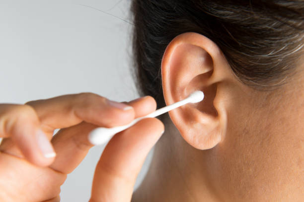 An image showing a person gently massaging their ear to remove earwax, as an alternative to using cotton swabs or ear candling for how to massage earwax out".