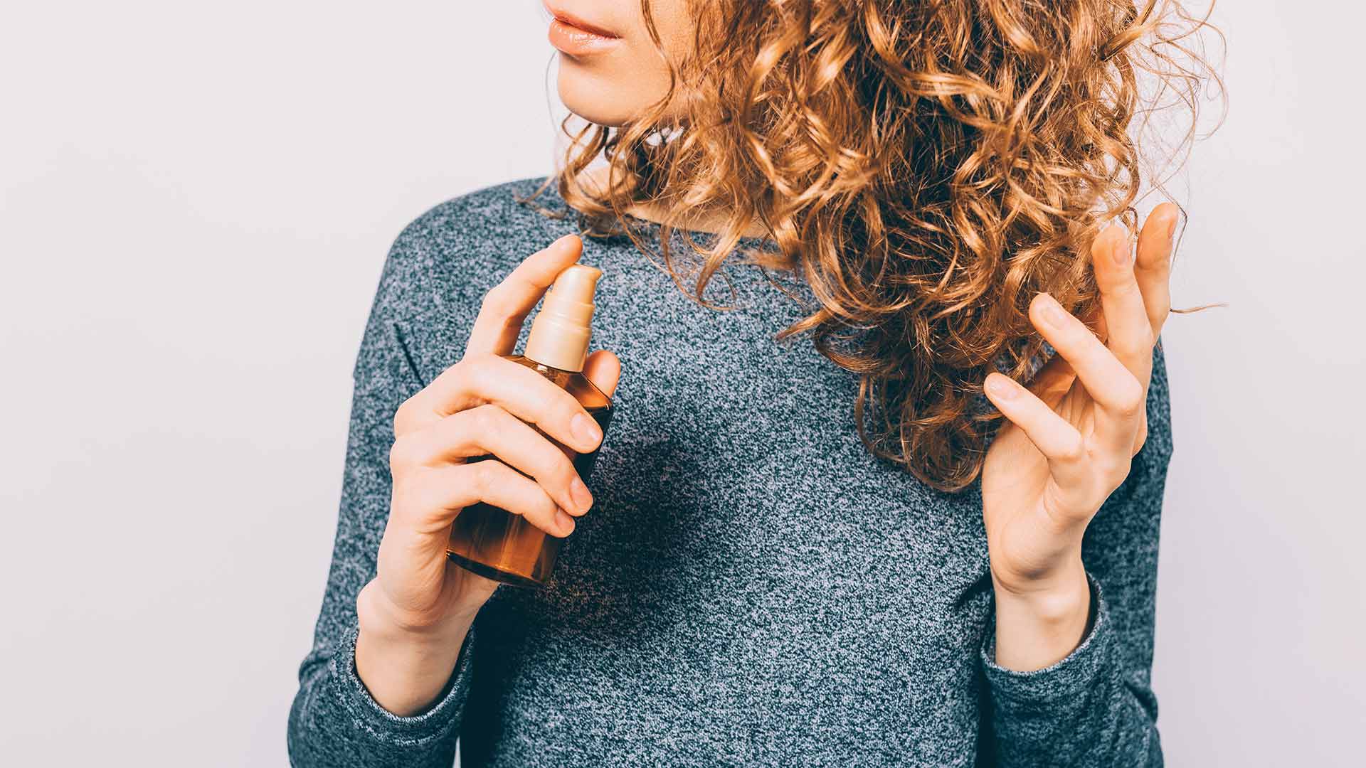 A woman spraying hair serum on her hair.