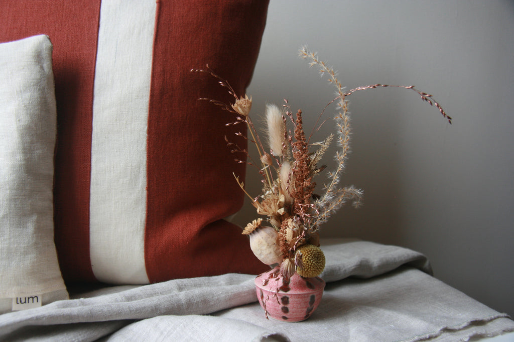 A rust-coloured red squirrel cushion with a small vase of dried flowers in front of it. 