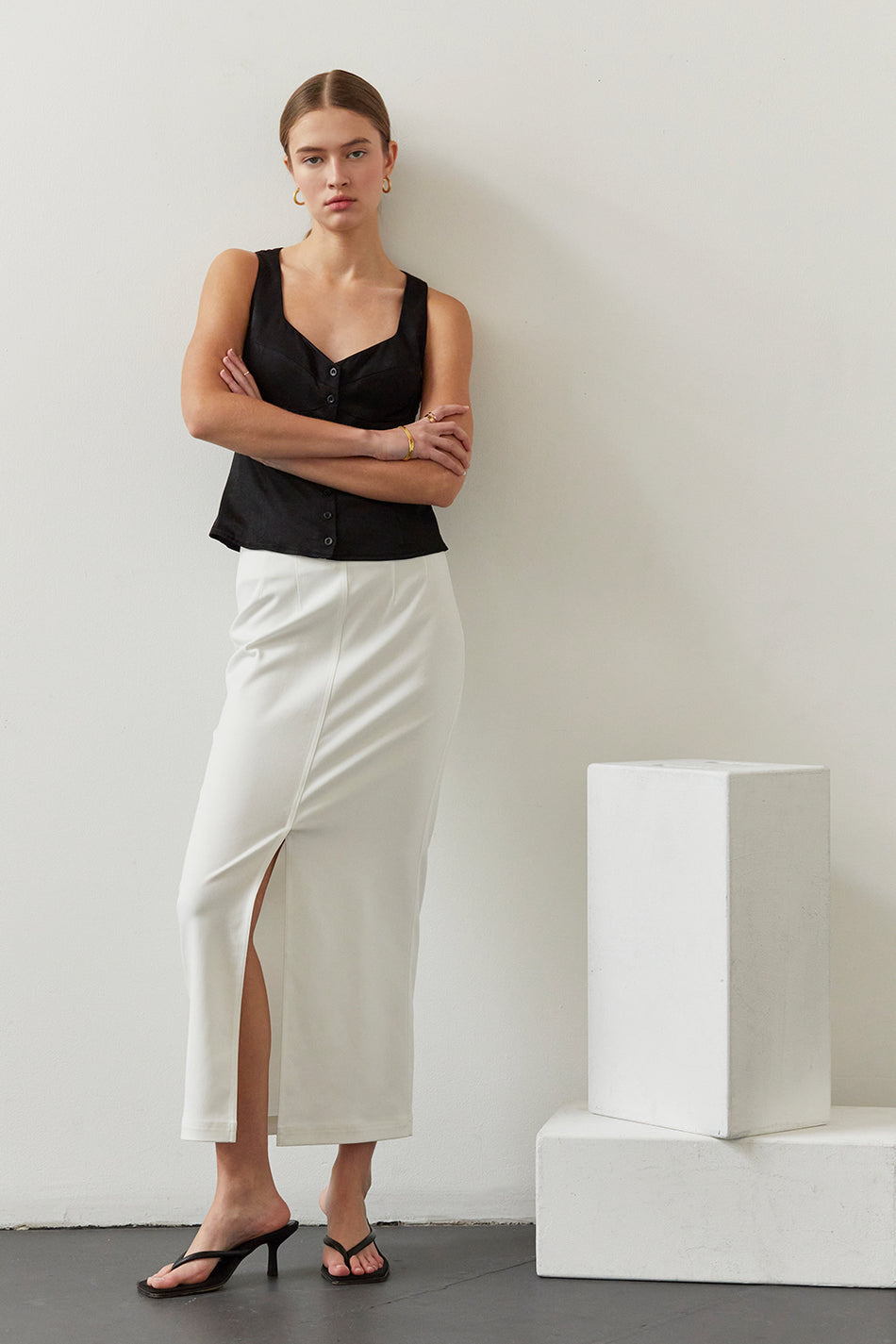 a model in a black sleeveless top and a white midi skirt