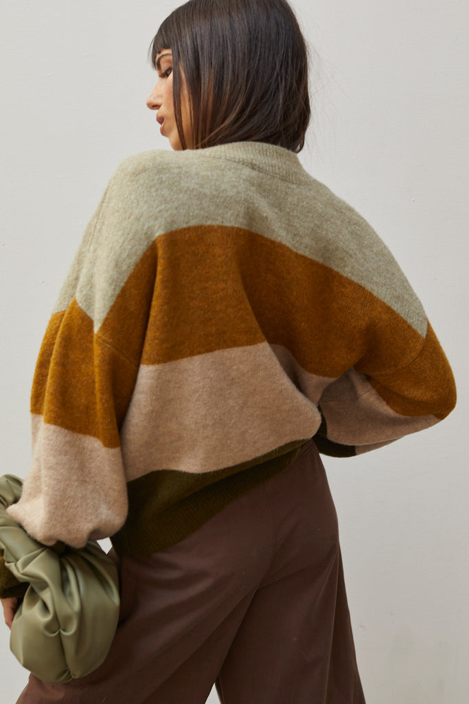 A woman wearing an olive multi color blocked sweater.