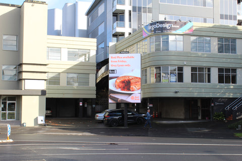 Roti Bros billboard on College Hill. Image of Butter Chicken Roti Pie cut open. Words on screen: Roti Pies now available at Farro Grey Lynn.