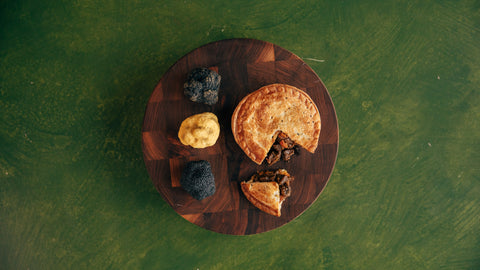 Birds eye view of truffle and beef cheek truffle pie on a circular chopping board on a dark green background