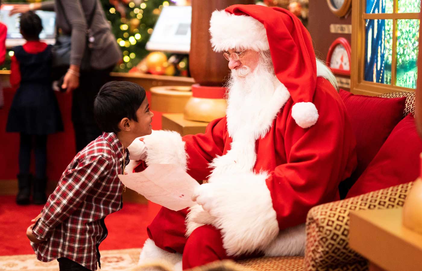 image of Santa Claus sitting down on a chair giving a gift to a child 