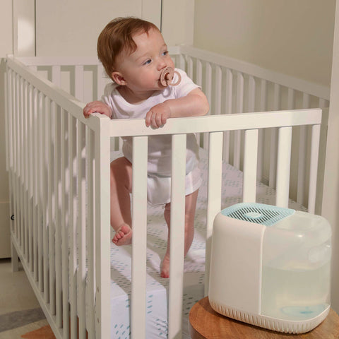 Baby standing in crib next to Canopy Nursery Humidifier